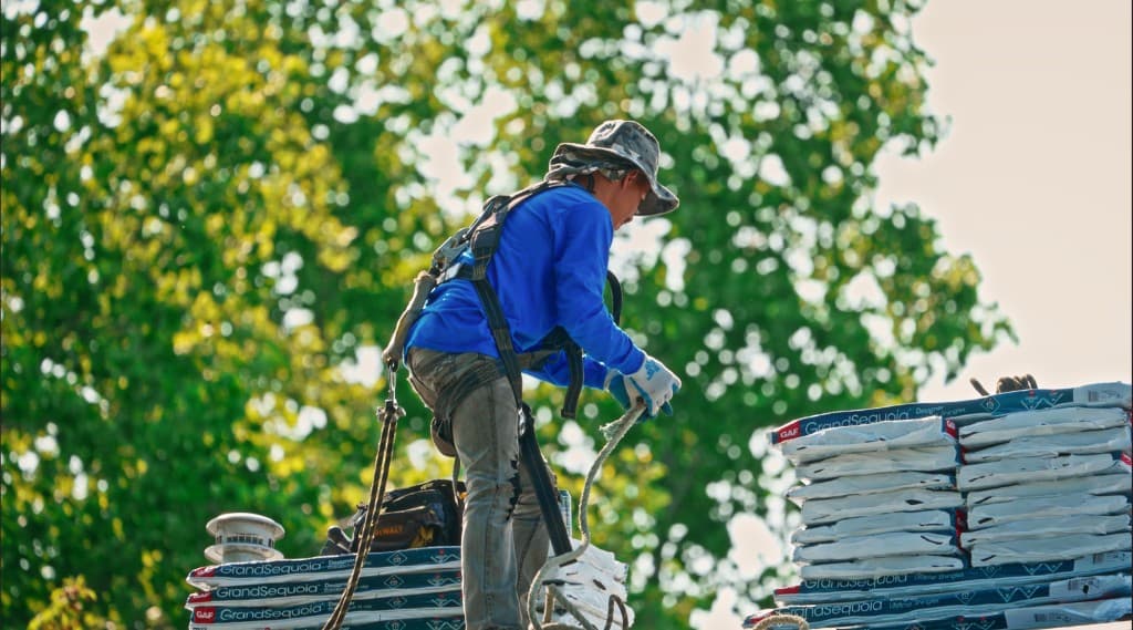 Roofer installing GAF Grand Sequoia designer shingles on a Kennewick roof, wearing a safety harness