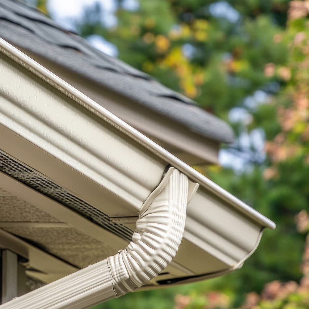 Close-up of cream K-style gutter and downspout elbow on a shingled roof
