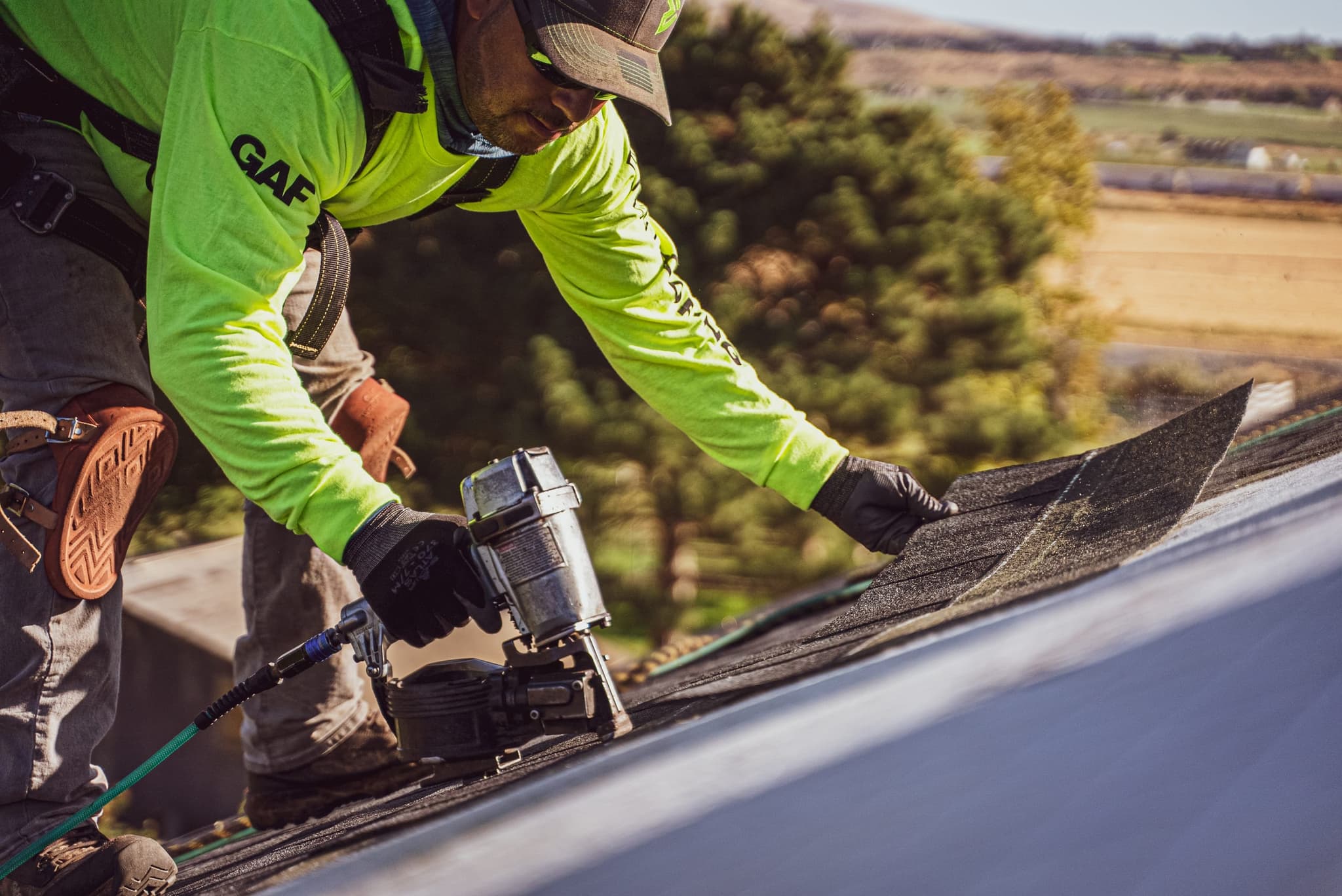 Roofer working on a steep-slope asphalt roof against a clear sky