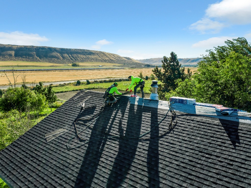 Eminent Roofing crew installing asphalt shingles on a roof with Eastern Washington hills beyond the eave